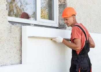 Insulation of the house with polyfoam. The worker is checking with an aluminum plaster ruler the accuracy of the installation a polystyrene board on the facade.