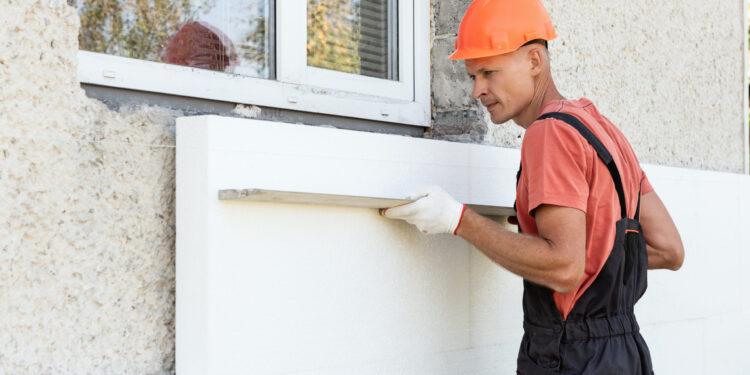 Insulation of the house with polyfoam. The worker is checking with an aluminum plaster ruler the accuracy of the installation a polystyrene board on the facade.