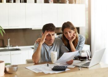 Unhappy American couple managing home accounts in kitchen, trying to save some money by cutting family expenses. Finances, bankruptcy, taxes, money, accounting and financial problems concept