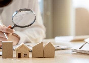 Looking for real estate agency, property insurance, mortgage loan or new house. Woman with magnifying glass over a wooden house at her office.