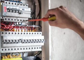 Man, an electrical technician working in a switchboard with fuses. Installation and connection of electrical equipment. Professional with tools in hand. concept of complex work, space for text. SSUCv3H4sIAAAAAAAEAI1Ry27DIBC8V+o/WJxjyS44dfoHPVTqPephgW2MQiDi0SqK8u8FEypOVW/szDK7s3N9fOg6wsErQV66a65SrbSOPjgIypoED5s77tBIdC2CUgXrFOgW5BDEYuCECTRR6wzfVpL4ACF69HnYHRIQ8JA0CvgrUTbal7qrxEqmH4ki72jPGsmmYXzkmXlTXqDWYNBGTyp/2/wh9mpktpyd/F+wPD6qbzigEZfVWmPZoUYolvellRy/A7pTewSIUtnG/5cVoHMDbZTOTgllDs03G5Y1j/pN2GiCyyuQaoNoa8/AdQ7jM2lixRfwPrXLijeDRDqFPTVzjA2rgbsqkSmzXI70aZwZm9g4Pm/pPLCB1JytOCrZWizRLypR7tLgKm9AKBspbjnrd9M09IzKqd9tJeufZ05nKjgIBunwtx9tVYW8sQIAAA==