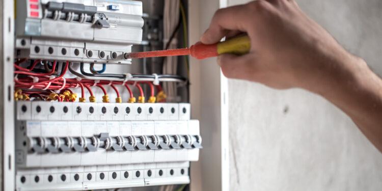 Man, an electrical technician working in a switchboard with fuses. Installation and connection of electrical equipment. Professional with tools in hand. concept of complex work, space for text. SSUCv3H4sIAAAAAAAEAI1Ry27DIBC8V+o/WJxjyS44dfoHPVTqPephgW2MQiDi0SqK8u8FEypOVW/szDK7s3N9fOg6wsErQV66a65SrbSOPjgIypoED5s77tBIdC2CUgXrFOgW5BDEYuCECTRR6wzfVpL4ACF69HnYHRIQ8JA0CvgrUTbal7qrxEqmH4ki72jPGsmmYXzkmXlTXqDWYNBGTyp/2/wh9mpktpyd/F+wPD6qbzigEZfVWmPZoUYolvellRy/A7pTewSIUtnG/5cVoHMDbZTOTgllDs03G5Y1j/pN2GiCyyuQaoNoa8/AdQ7jM2lixRfwPrXLijeDRDqFPTVzjA2rgbsqkSmzXI70aZwZm9g4Pm/pPLCB1JytOCrZWizRLypR7tLgKm9AKBspbjnrd9M09IzKqd9tJeufZ05nKjgIBunwtx9tVYW8sQIAAA==