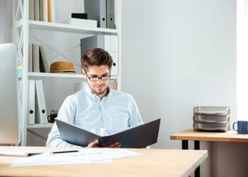 Concentrated young businessman working with documents in folder at workplace