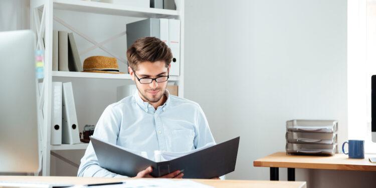 Concentrated young businessman working with documents in folder at workplace