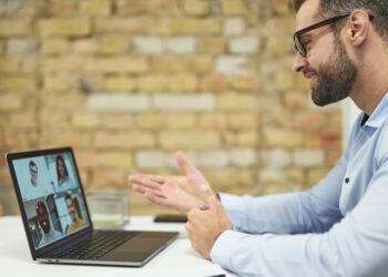 Friendly young entrepreneur smiling and gesturing while conducting the online meeting with employees